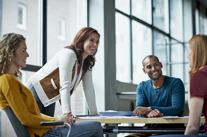 Coworkers in meeting lead by a woman standing and leaning over the table with both hands on the table